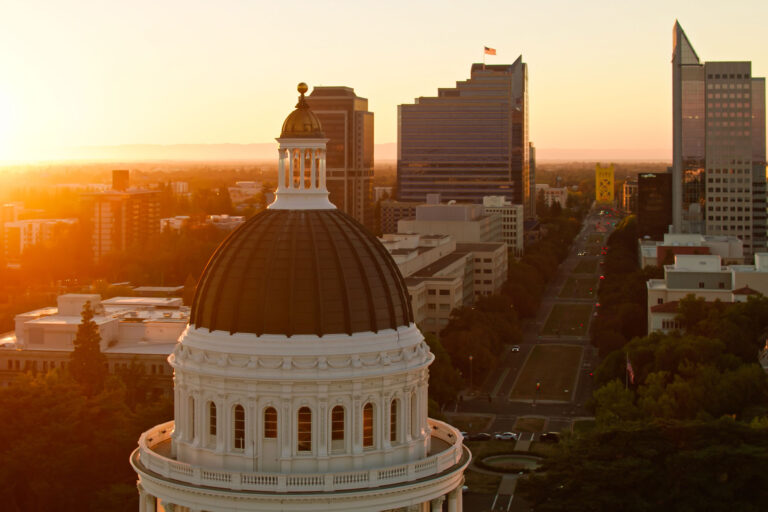 photo - Drone Shot of California State Capitol with Setting Sun and Tower Bridge in the Distance