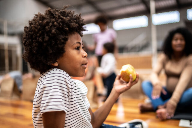 photo - Child Eating an Apple and Sitting on Floor of Community Center