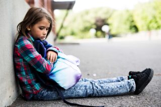 photo - Elementary School Girl Looking Down and Sitting on School Yard Alone