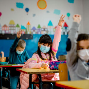 photo - Elementary School Students Raising Hands and Wearing Masks in Classroom
