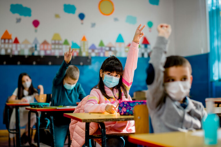 photo - Elementary School Students Raising Hands and Wearing Masks in Classroom
