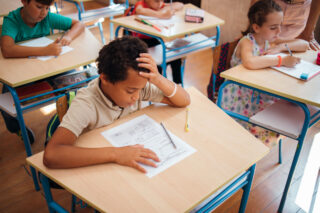 photo - Elementary Schoolboy in Classroom Sitting at Desk and Having Trouble with a Test