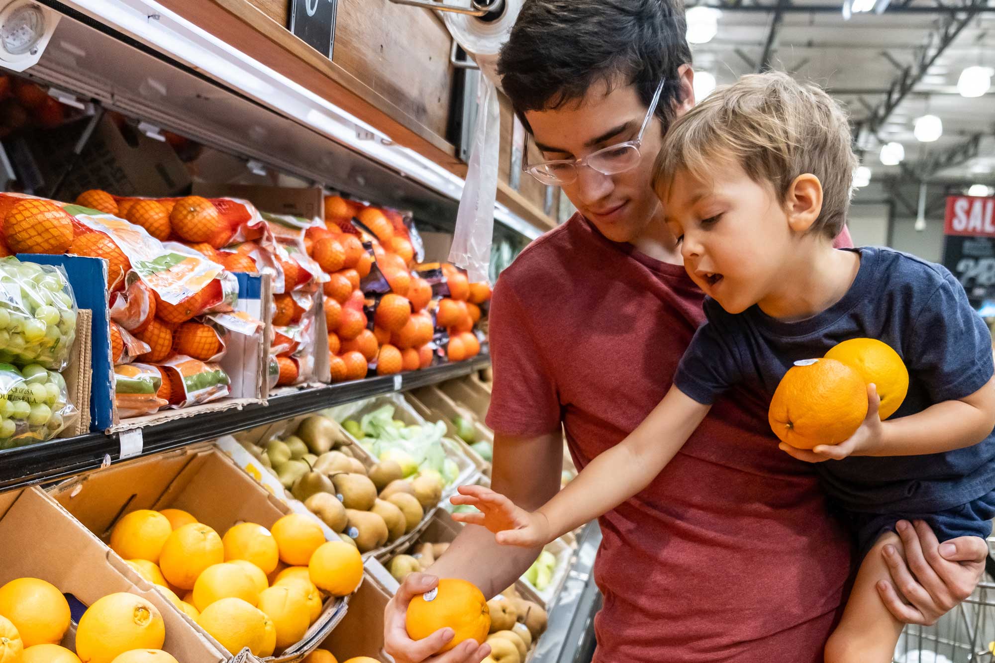 photo - Father Holding Young Son as They Pick Fruit at Grocery Store