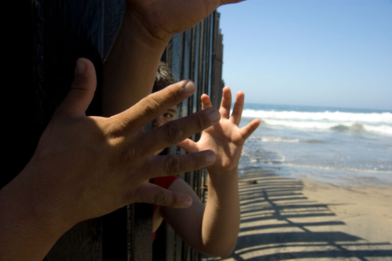 photo - Hands and a Child's Face Poking through Border Fencing