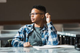 photo - Male Student Sitting in Classroom with Notebook and Pen Looking to Right