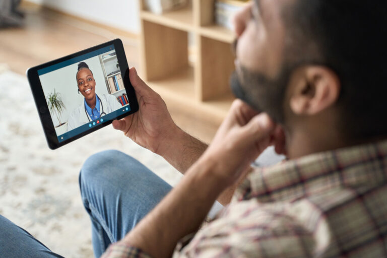 photo - Man at Home Holding Device on Telehealth Appointment with Doctor
