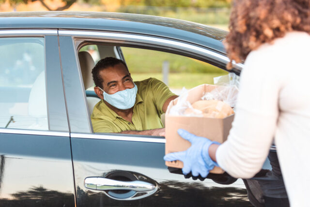 photo - Man in Car Wears Mask While Receiving Box of Food
