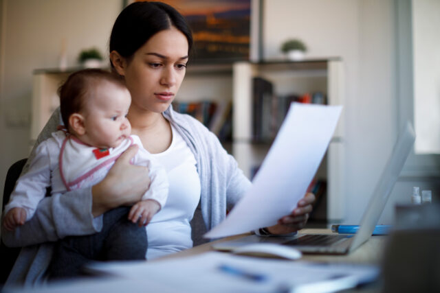 photo - Mother Working on Paperwork at Home and Holding Baby