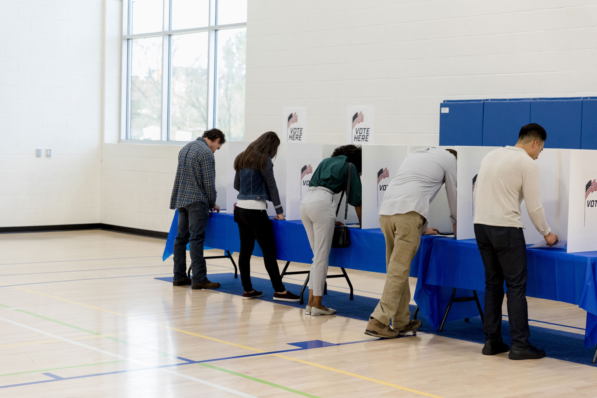 photo - People Stand at Voting Booths Along Gym Wall