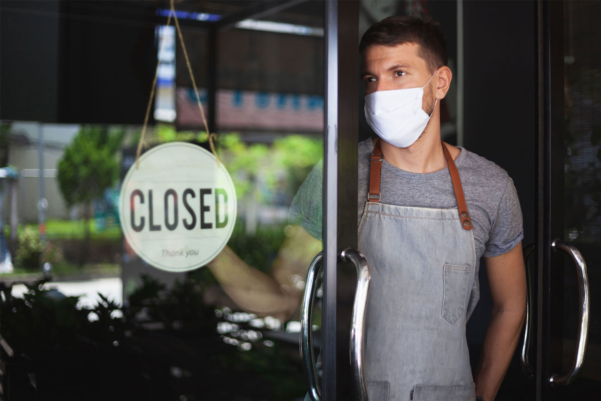 photo - Restaurant Worker Wearing Mask and Hanging Closed Sign on Door