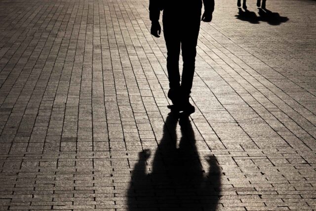 photo - Silhouette and Shadow of Man Walking Towards Couple at Night