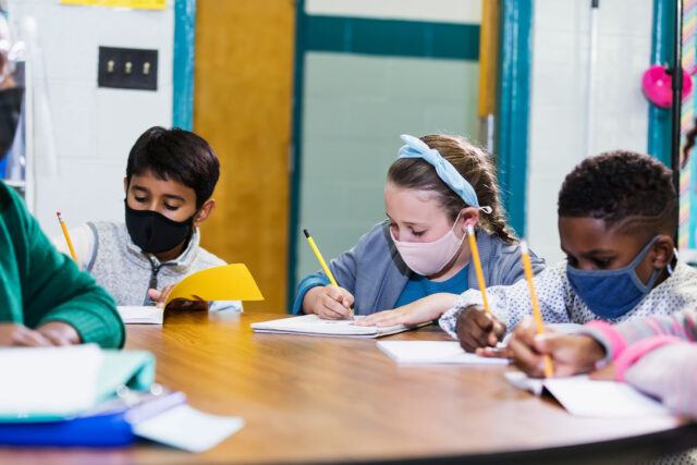 photo - Teacher and Students at Center Table in Classroom Wearing Masks