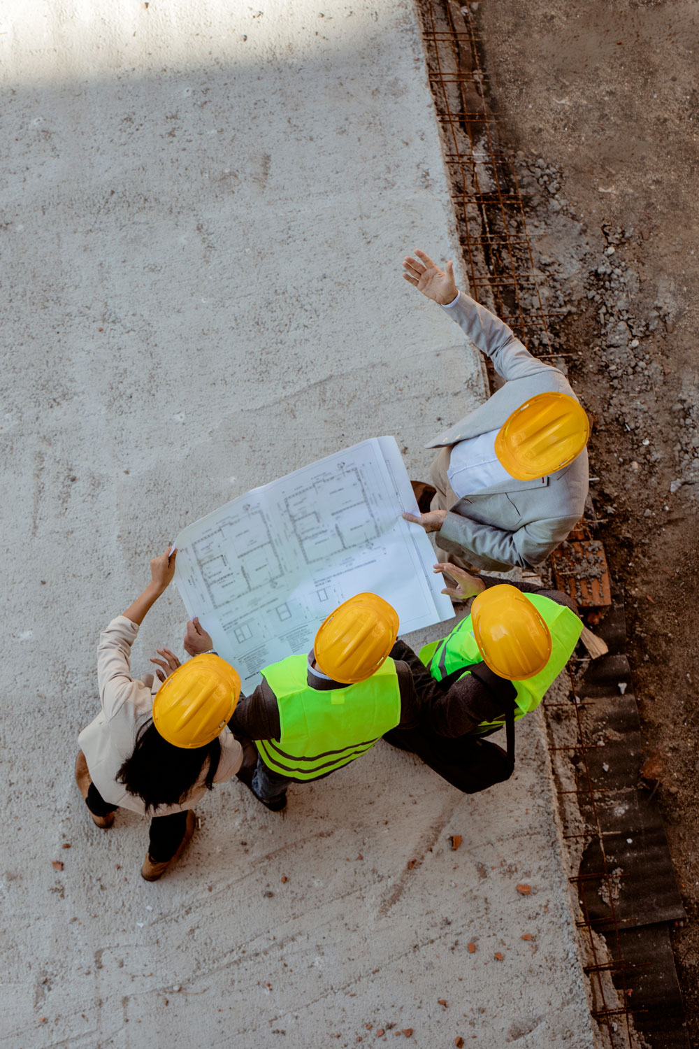 photo - Top View of Architects and Engineer Workers with Blueprints Discussing at Construction Site