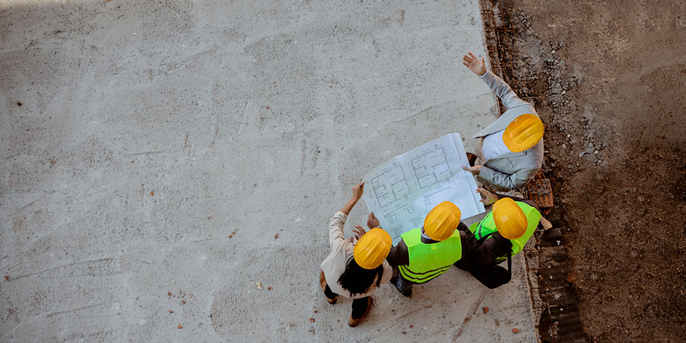 photo - Top View of Architects and Engineer Workers with Blueprints Discussing at Construction Site